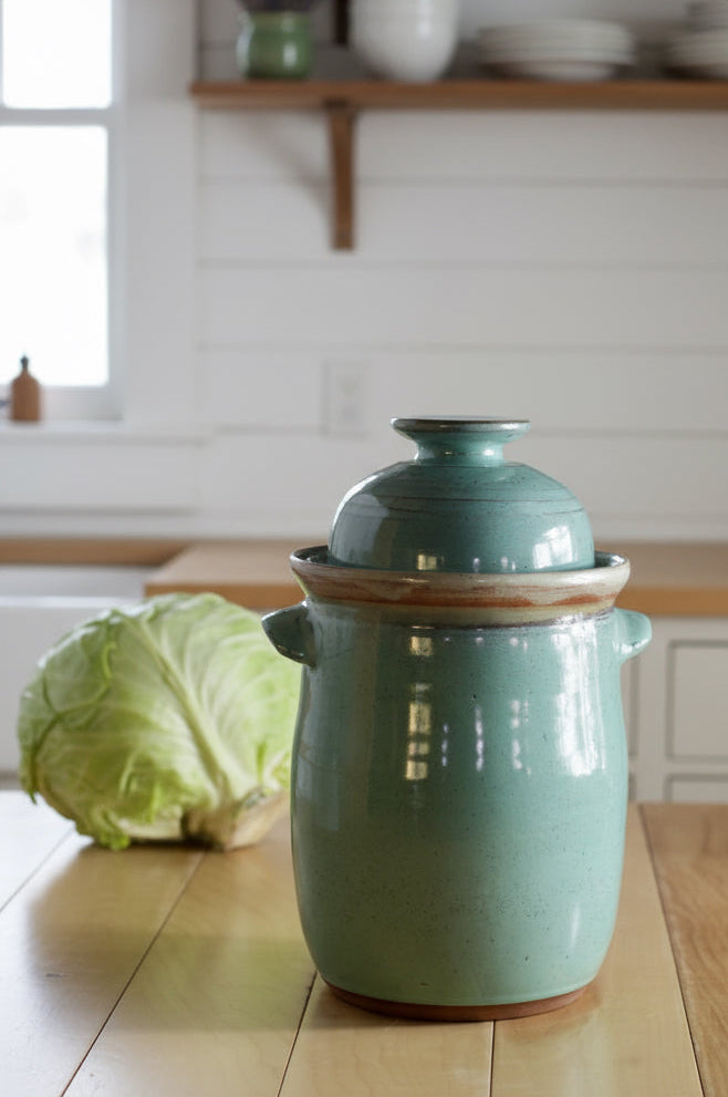 Green ceramic jar with wooden lid on a wooden table in a kitchen setting