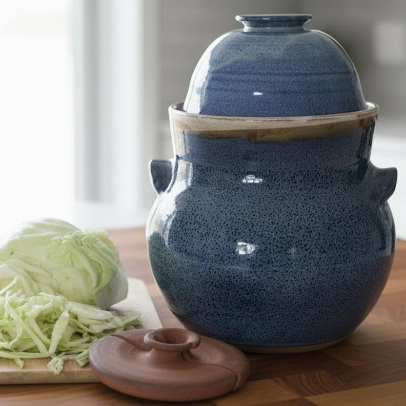 Blue ceramic jar with a lid on a wooden surface next to a cutting board with shredded cabbage.
